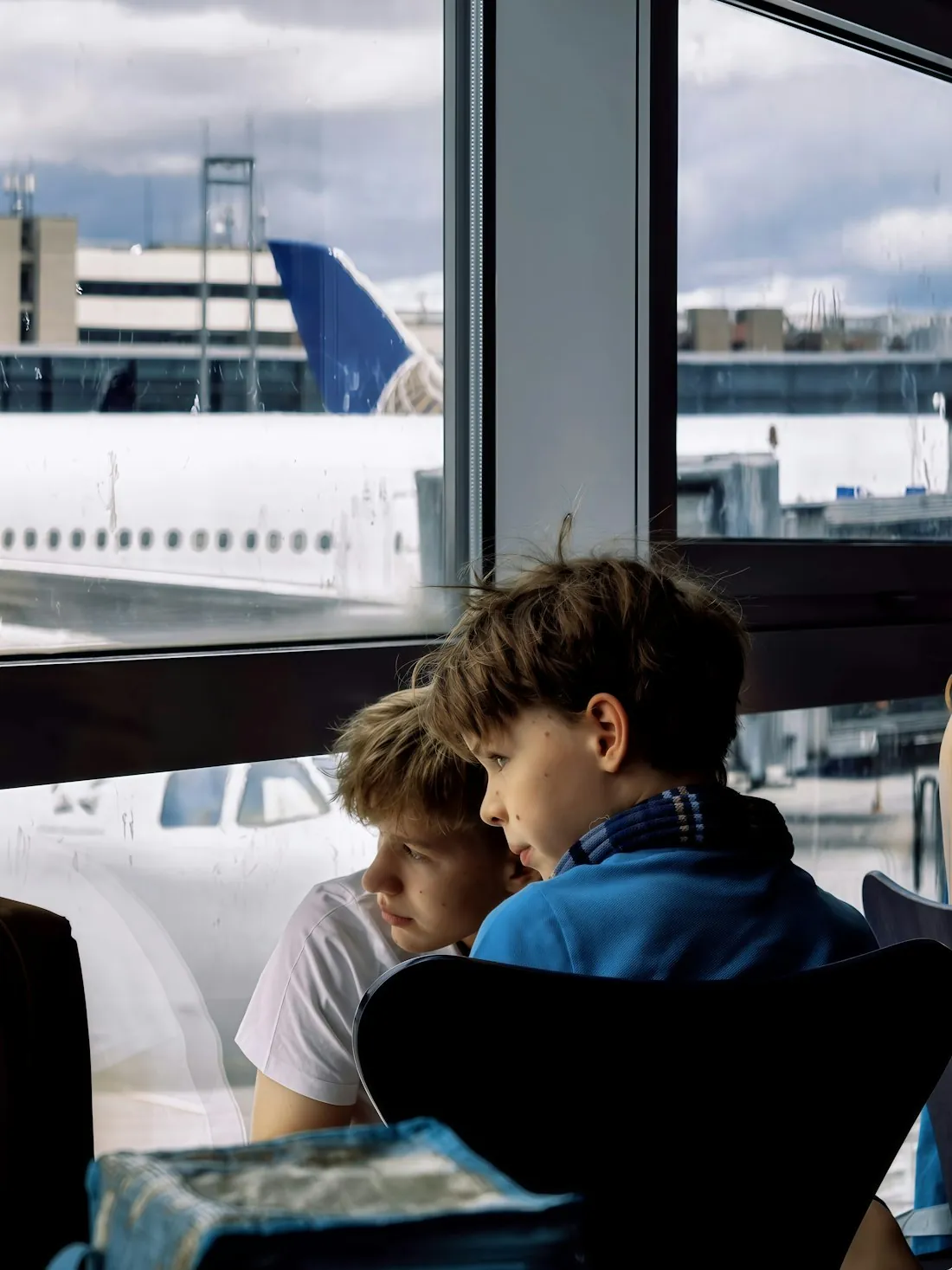 Two children watching an airliner's tail and fuselage from the terminal window